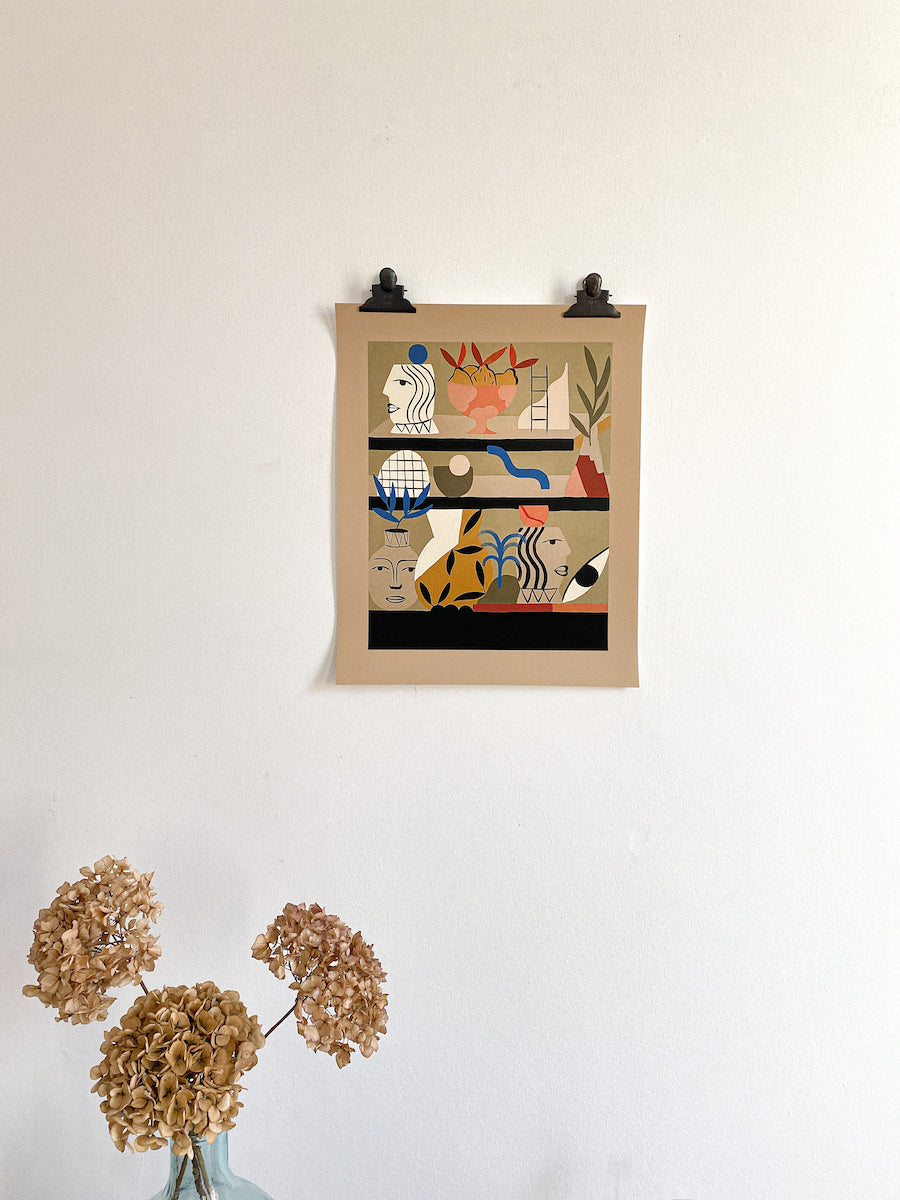Madi print of vases, faces and plants on beige paper with thick border hanging on wall. Dried hydrangea vase in bottom left corner