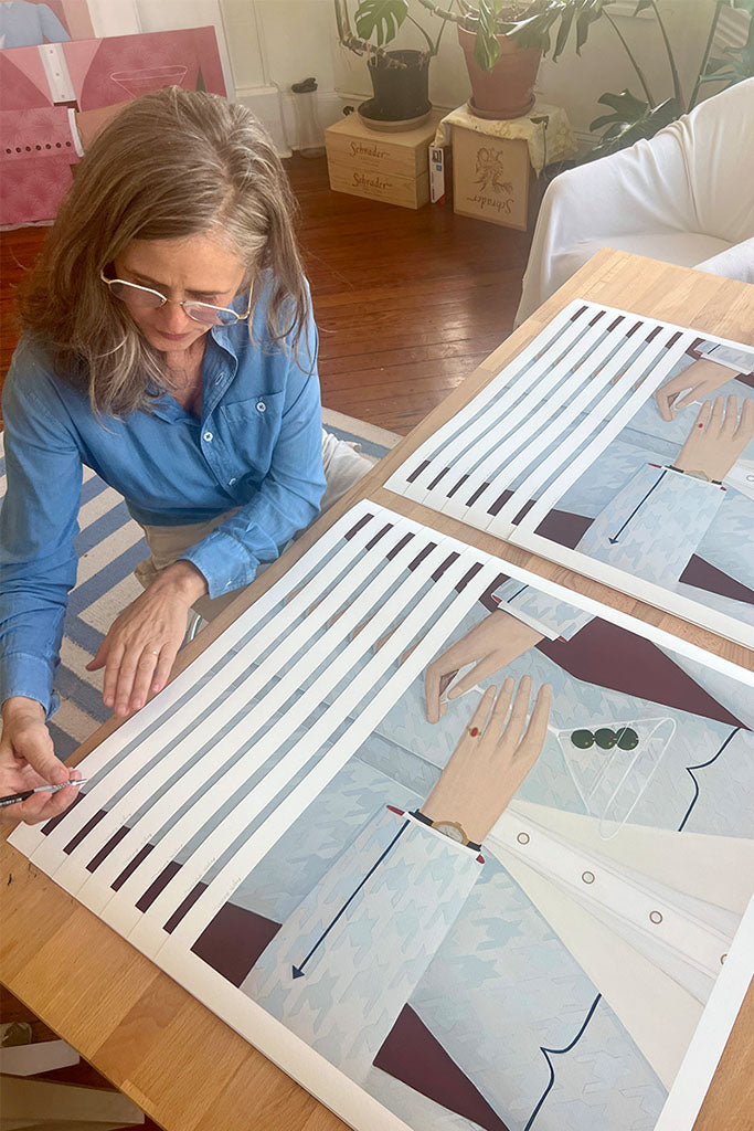 Angela Burson signing prints of  figure holding martini glass in patterned shirt