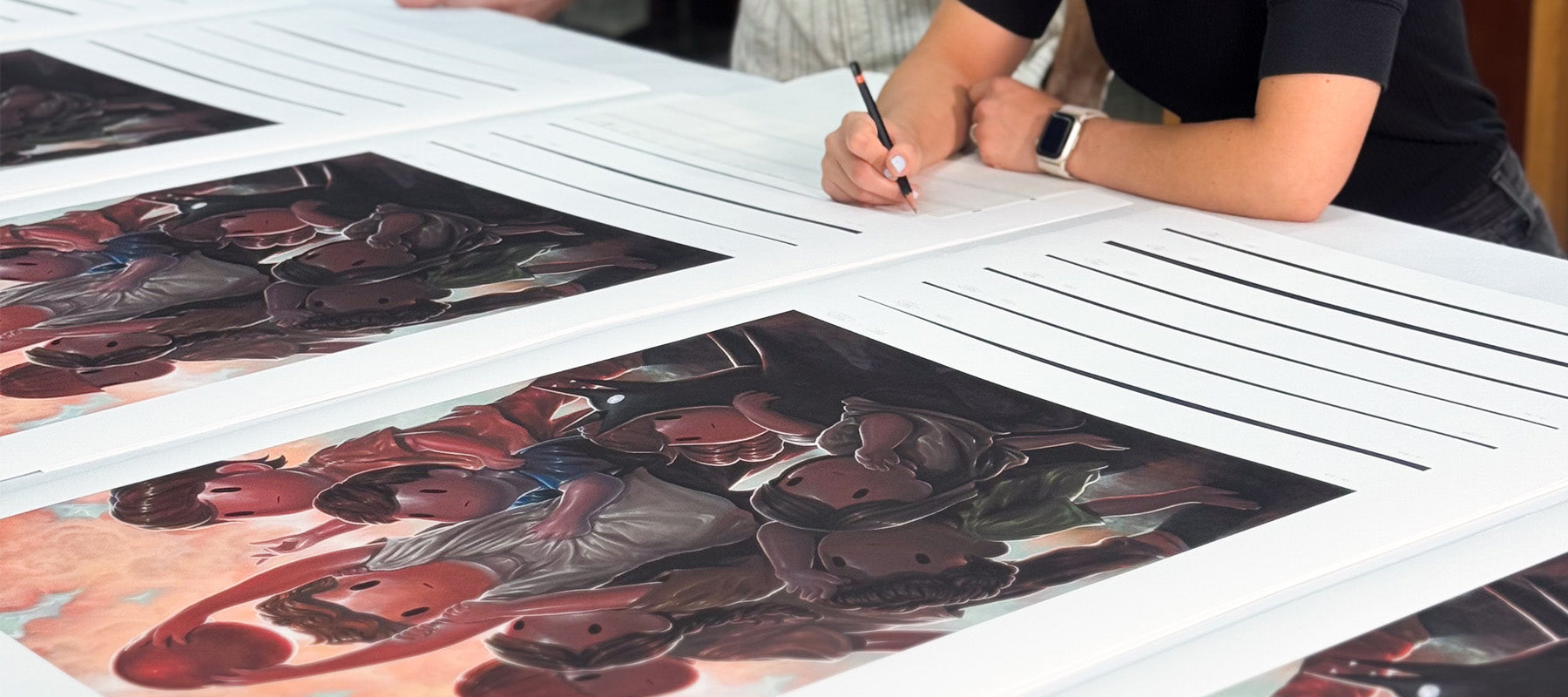 Person signing prints of children playing dodgeball on a table