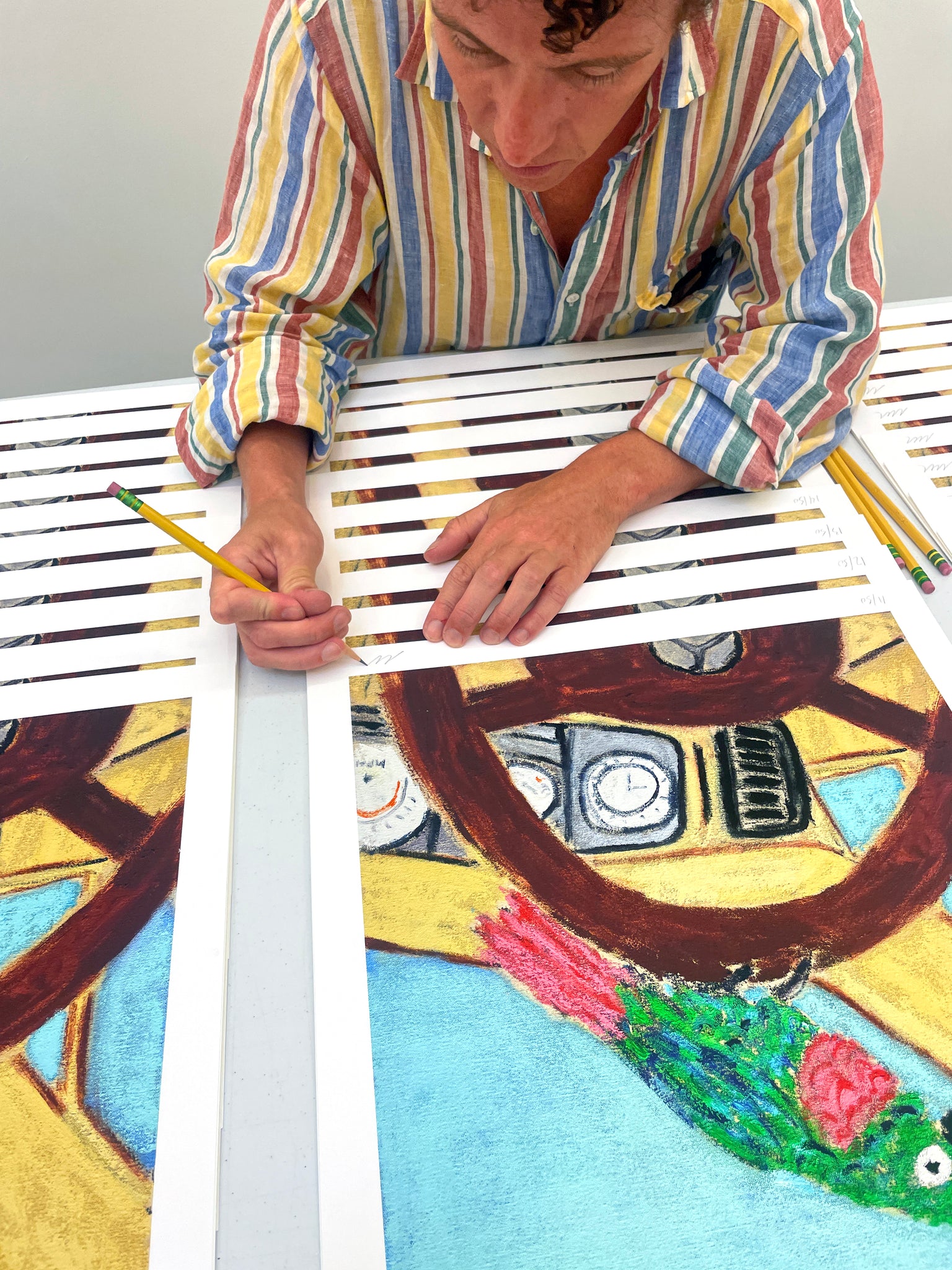 Michael McGregor wearing striped shirt signing print of small colorful bird on the steering wheel of a car