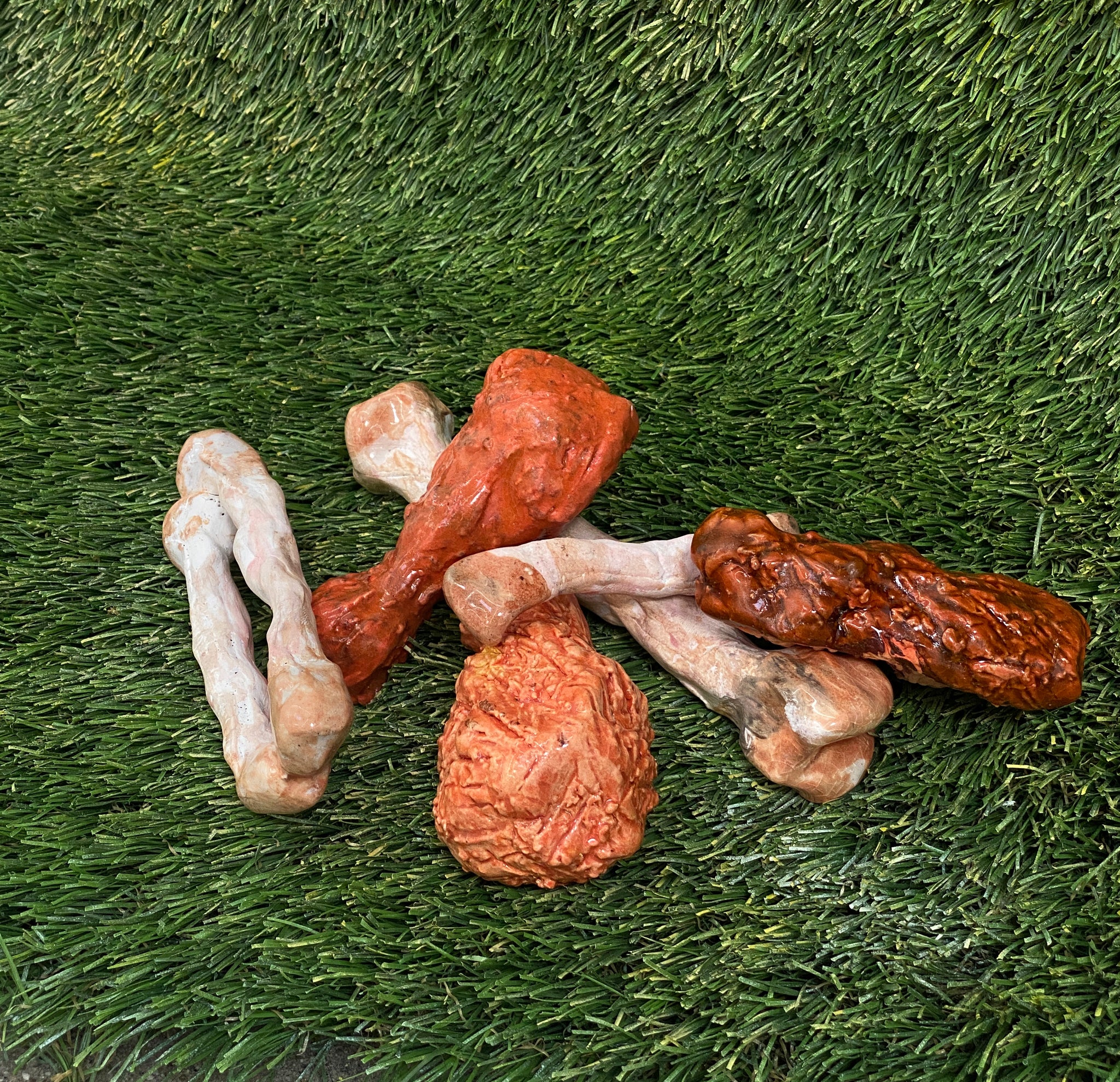 Ceramic sculptures of chicken wings and chicken bones on fake grass