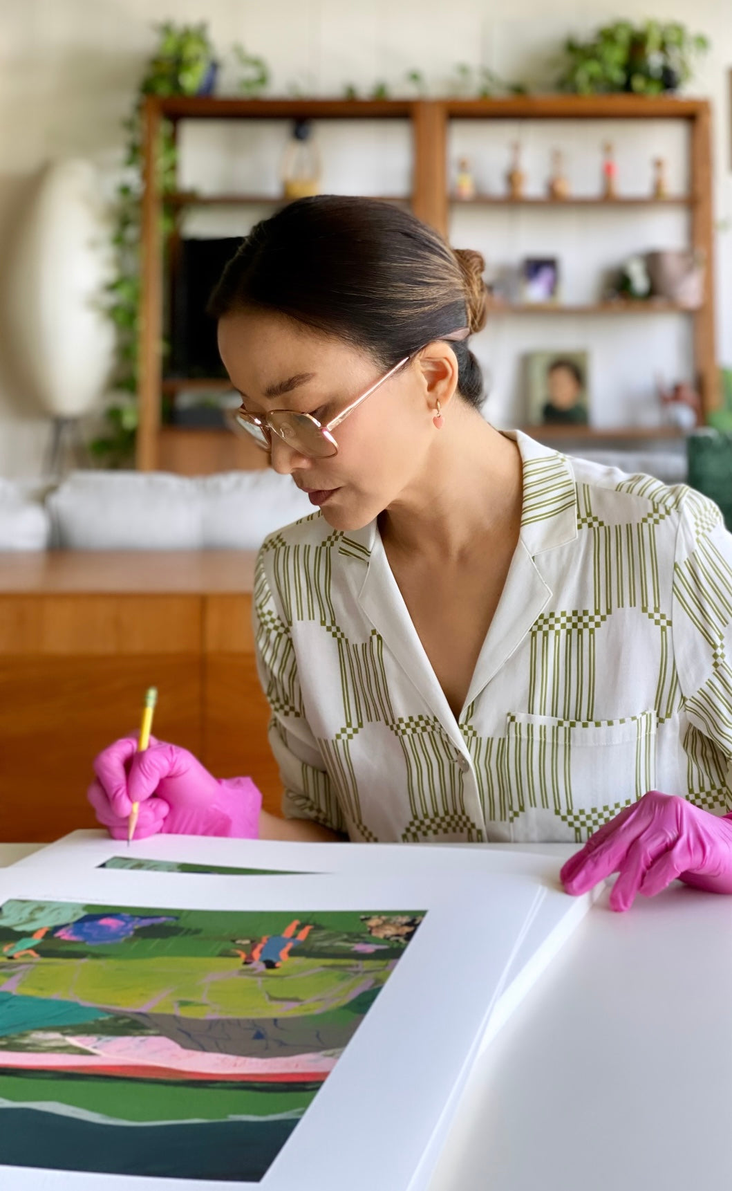 Seonna Hong (woman in glasses with hair pulled back) signing prints while wearing pink gloves