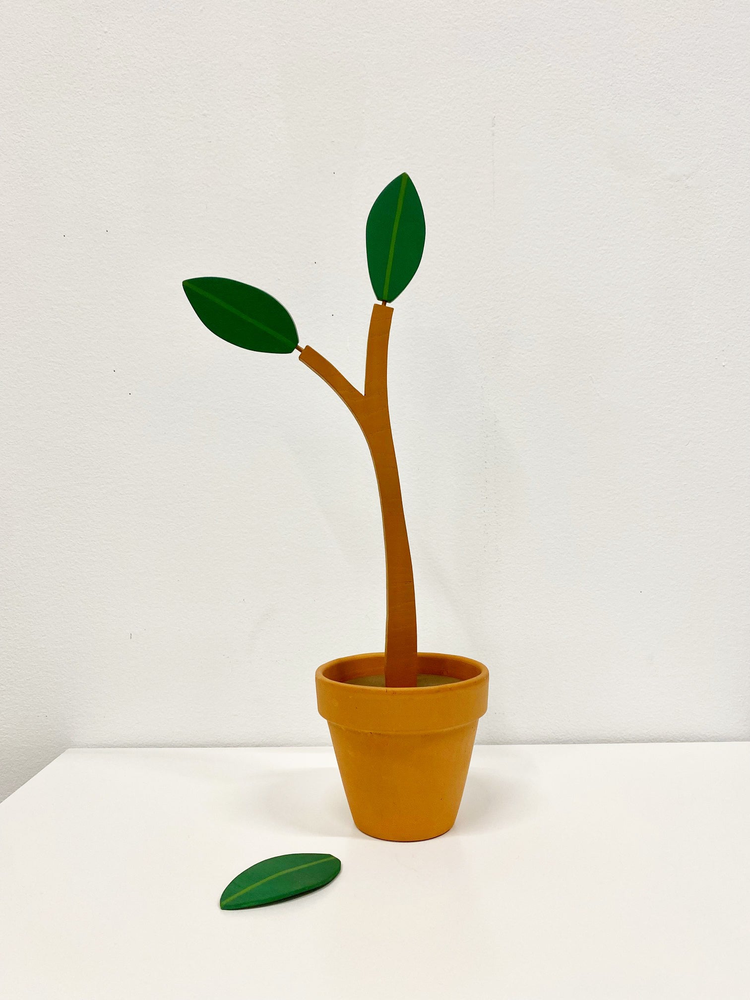 Wooden sculpture of plant with three leafs that one fell off in a terracotta pot