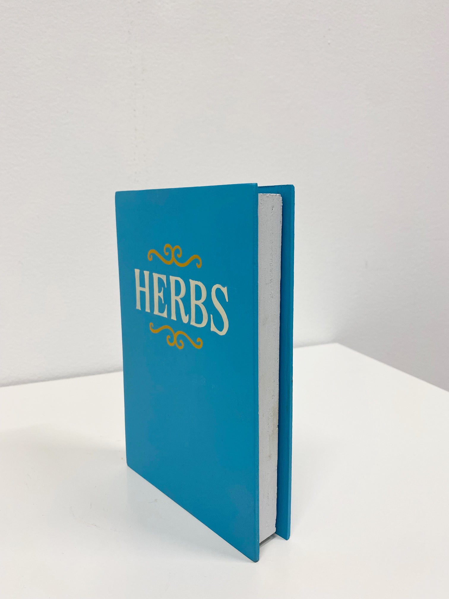 Wooden sculpture of a blue book with the word "Herbs" on the front