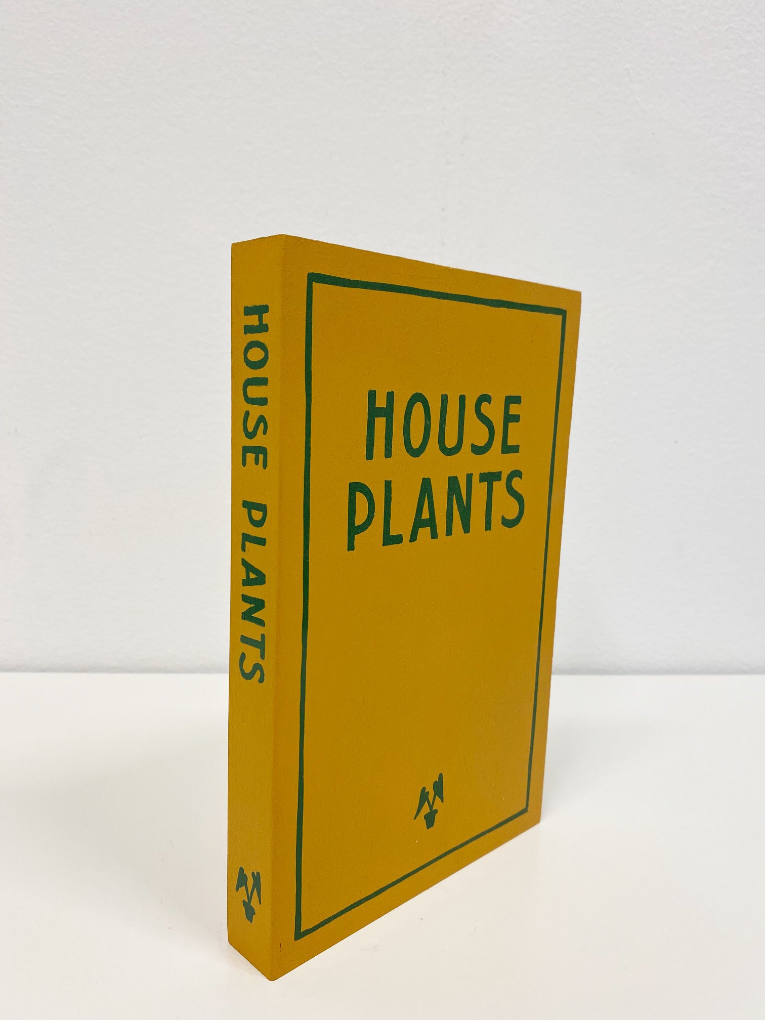 Wooden sculpture of a yellow book with the works House Plants painted on the front and on the spine of the book in dark green