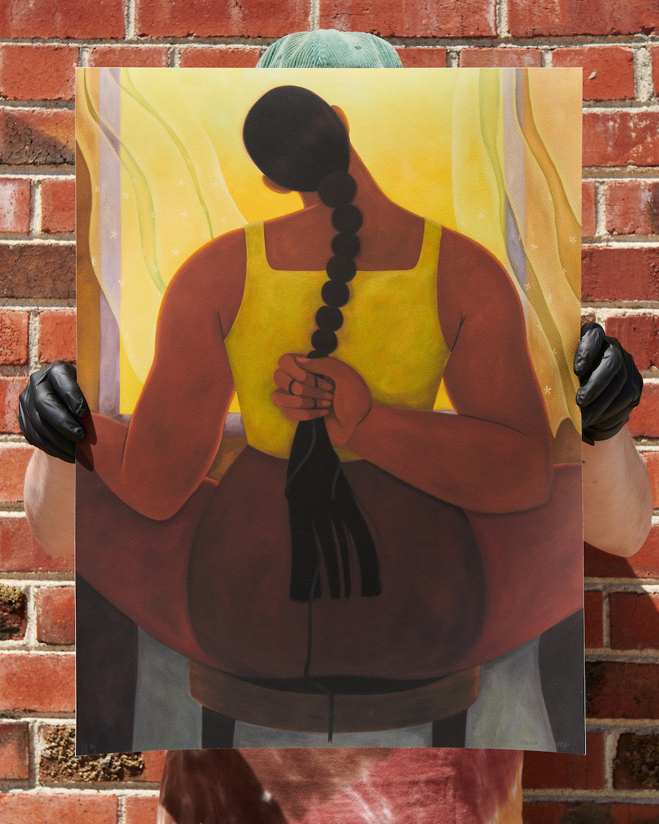 person standing behind print image and holding it up from the sides in front of a brick wall