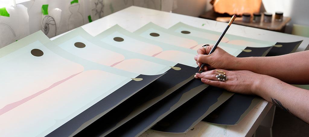 abstract black and green landscape print being signed by hands adorned with rings